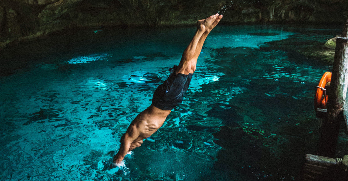 Man diving headfirst into a clear, blue natural swimming hole.