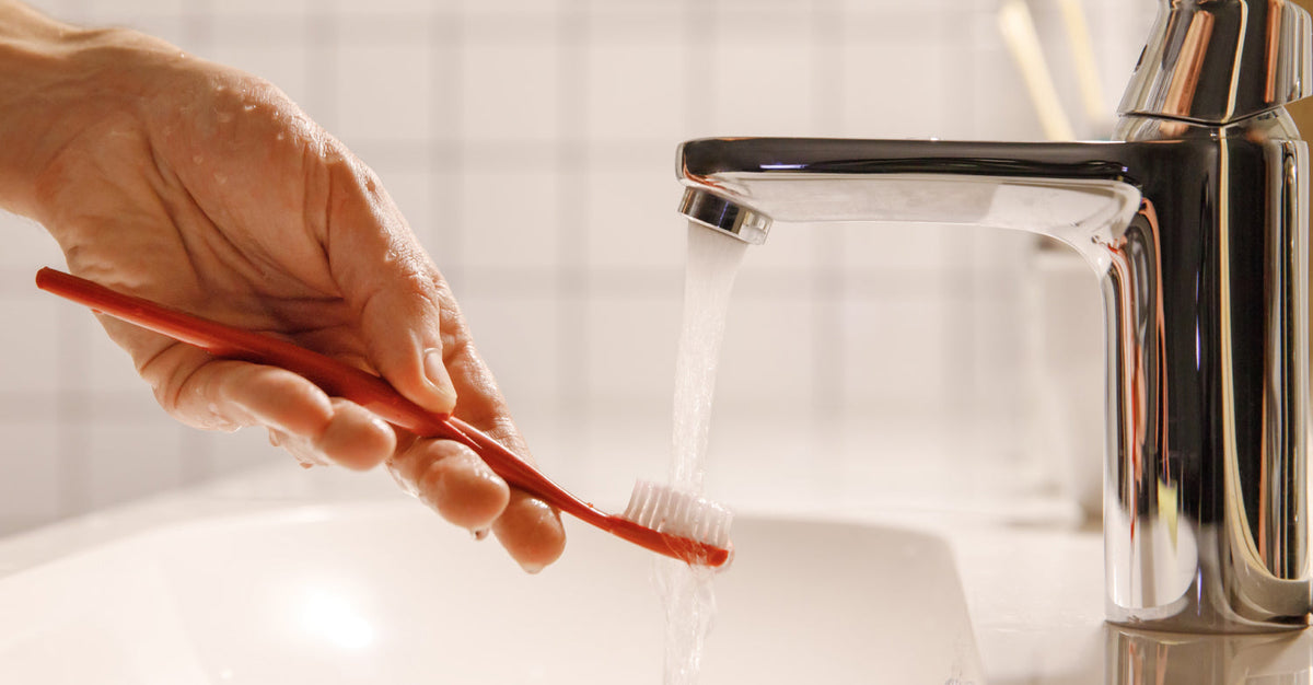 Hand rinsing a toothbrush under running water.