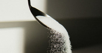 Spoon pouring granulated sugar with sunlight casting a shadow.