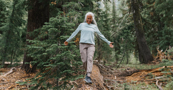 A joyful older woman balancing on a fallen log in a forest, representing physical agility and healthy aging