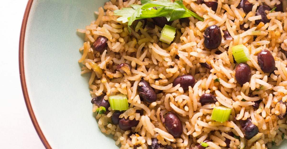 Close-up of a bowl filled with cooked rice and black beans, garnished with chopped green onions and cilantro.