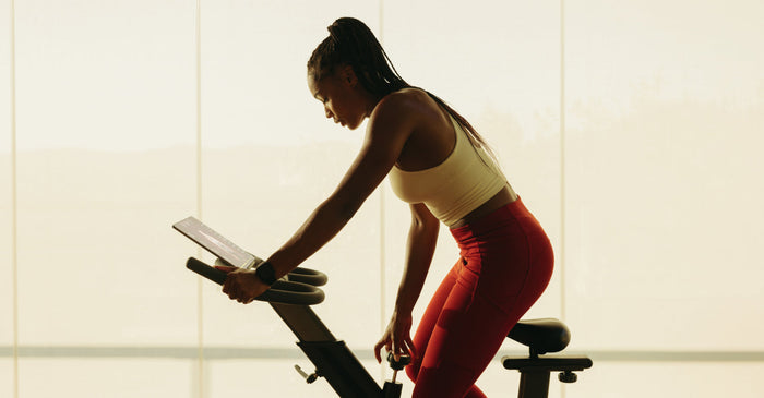 Person leaning forward on a stationary bike during an indoor workout with soft natural light behind them.