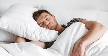 Man sleeping peacefully in bed, wrapped in white bedding, illustrating healthy sleep patterns aligned with the circadian rhythm.