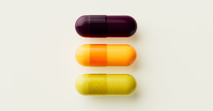A close-up studio shot of three Tally Health capsules lined up on a plain background: a deep purple capsule, a two-tone orange and yellow capsule, and a light green capsule.