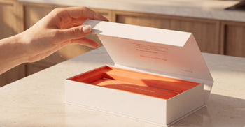 A hand opening a white Tally Health test kit box with an orange interior on a kitchen counter.