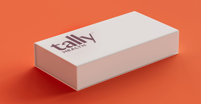 A clean, minimalistic shot of a white Tally Health box with the company logo on a vibrant orange background. This image highlights the product's packaging, suggesting a high-quality, modern health kit.