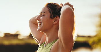 Woman in workout top smiling and tying her hair back outdoors at sunset