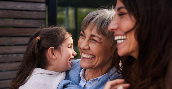Grandmother, mother, and young daughter smiling together, representing female longevity across generations.