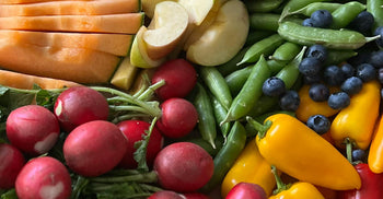 A colorful assortment of high-fiber fresh vegetables and fruits including cantaloupe, apple slices, snap peas, blueberries, radishes, and yellow mini peppers