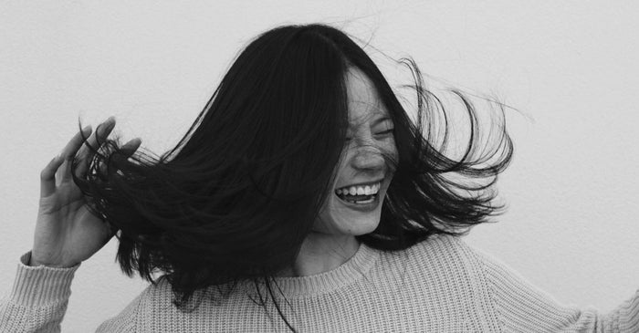 A joyful woman with long, dark hair laughs while tossing her hair, conveying healthy and vibrant hair. This black and white image emphasizes healthy hair.
