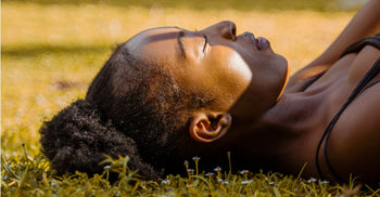 Close-up of a woman  lying on grass in golden sunlight, eyes closed, relaxed expression.