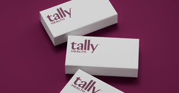 Three white Tally Health branded boxes with the Tally Health logo, arranged diagonally on a dark maroon background.