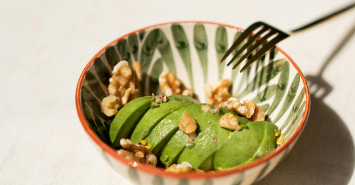 Sliced avocado topped with walnuts in a ceramic bowl, representing high-fat foods commonly eaten on a keto diet.