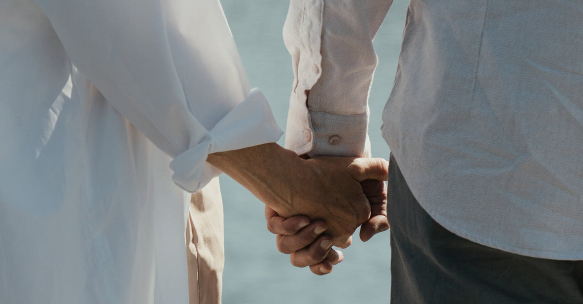 Close-up of two people holding hands near a body of water, symbolizing intimacy, trust, and long-term partnership.