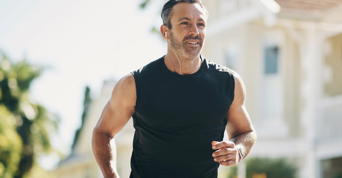 Middle-aged man jogging outdoors in a sleeveless black shirt and earbuds, demonstrating active lifestyle and muscle maintenance with age.