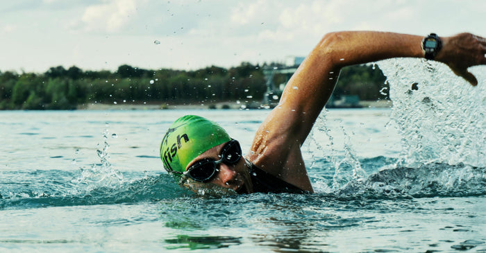 A determined swimmer in a green cap and goggles doing the crawl stroke in open water, demonstrating physical endurance, fitness, and athletic perseverance.