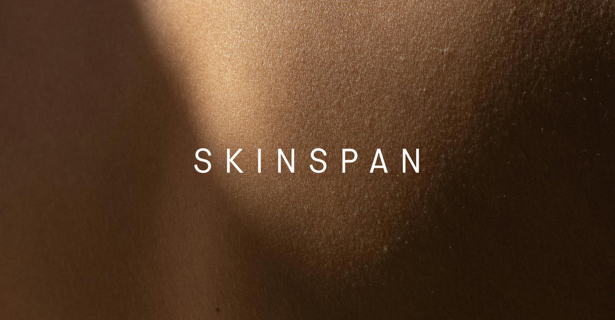 A macro photograph of smooth, evenly lit skin with the word “SKINSPAN” centered in white text.