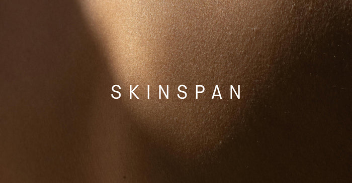 A macro photograph of smooth, evenly lit skin with the word “SKINSPAN” centered in white text.