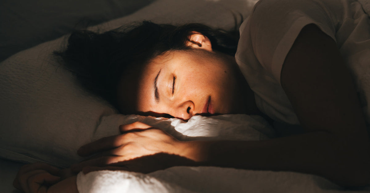 Woman sleeping peacefully in bed with sunlight streaming across her face and hands