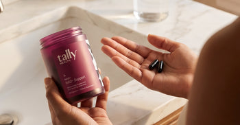 A hand holding NAD+ supplement from Tally Health in a bathroom.