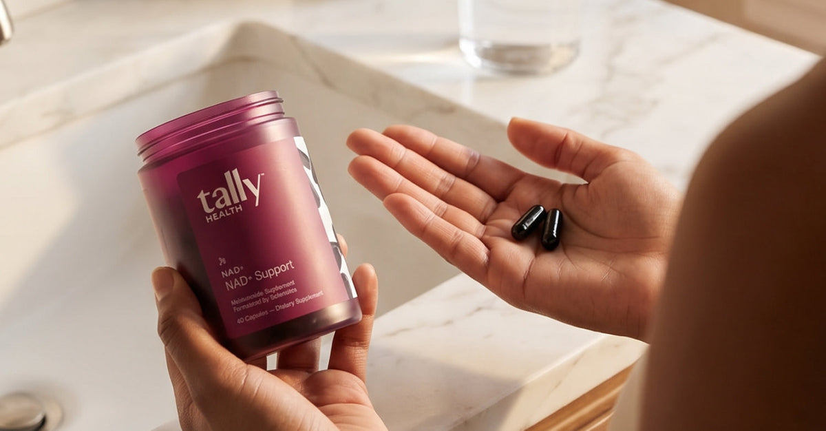 A hand holding NAD+ supplement from Tally Health in a bathroom.