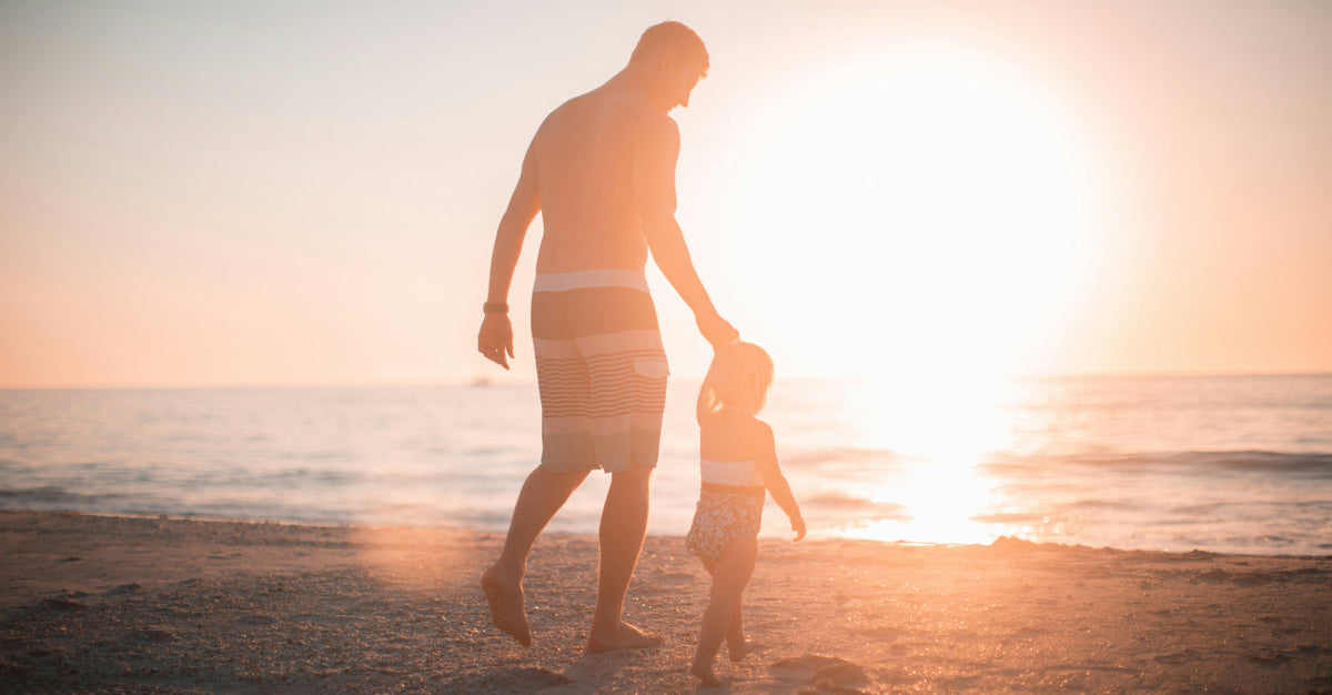 Silhouette of a parent and young child walking hand-in-hand along a beach at sunset