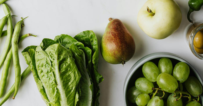 Fresh whole foods including romaine lettuce, green beans, pears, apples, and grapes arranged on a white surface, representing fruits and vegetables in a healthy diet.
