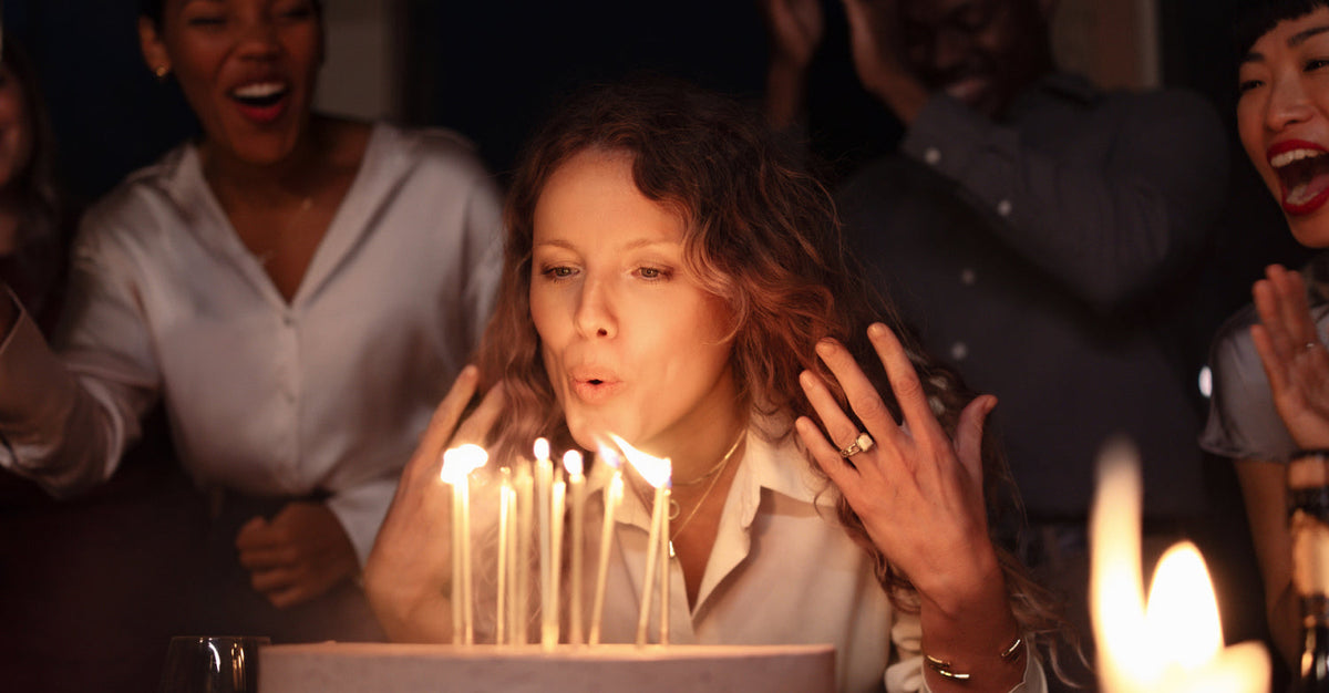 A woman surrounded by friends blowing out candles on a birthday cake, symbolizing the passage of time and the joy of aging well
