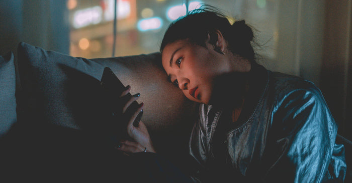 A person on a couch looking at their phone in a dimly lit room, with a soft, warm glow from the screen on their face. This image evokes a sense of late-night scrolling and screen time.