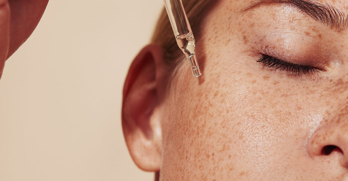 A close-up of a woman's face with a dropper of serum