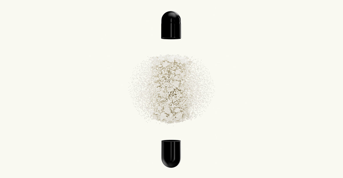 Black supplement capsule shown open, with fine white powder suspended between the two halves on a light background.