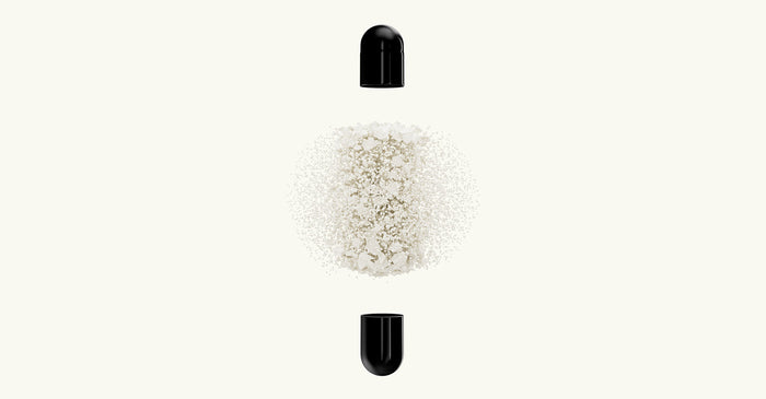 Black supplement capsule shown open, with fine white powder suspended between the two halves on a light background.